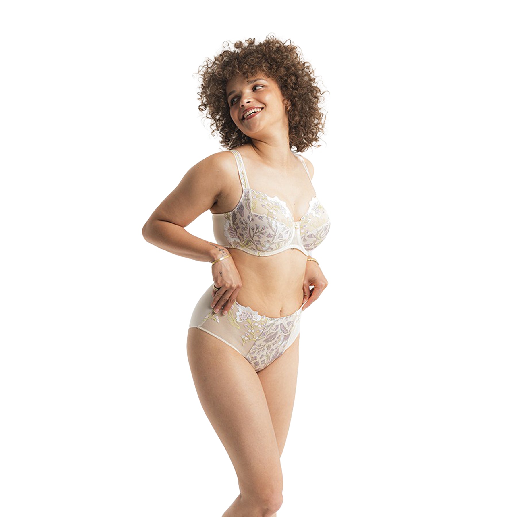 Model smiling and posing playfully in a sheer floral bra and brief set with full coverage, shown on white background.
