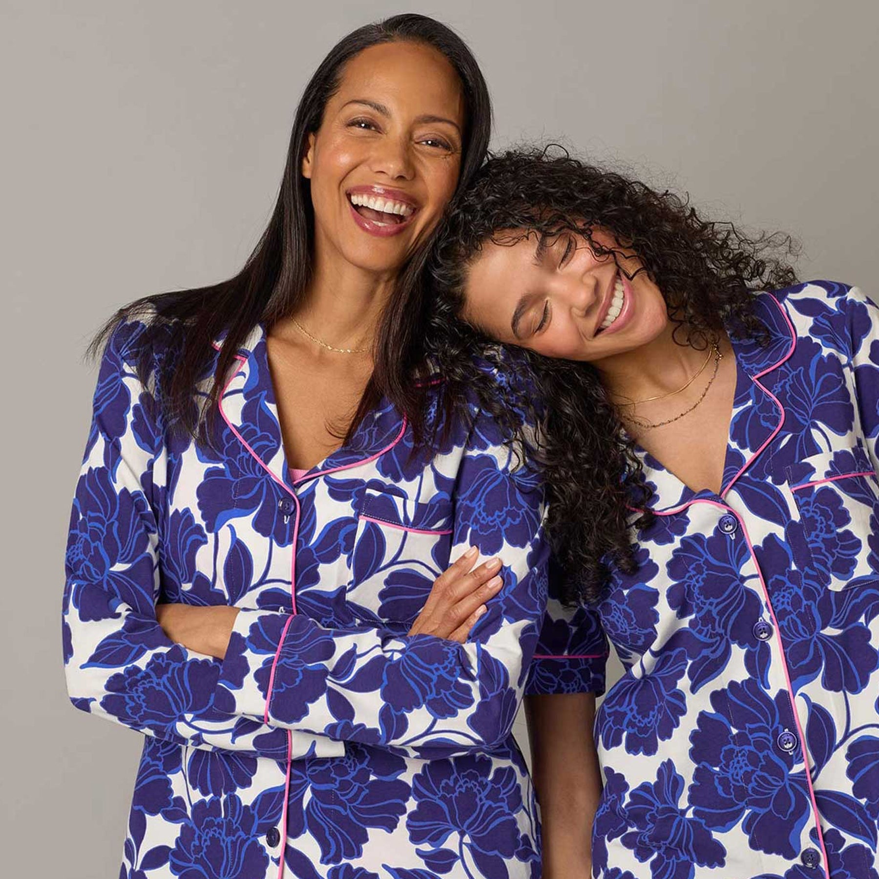 Two women smiling and wearing matching navy floral print pajamas with pink piping details.