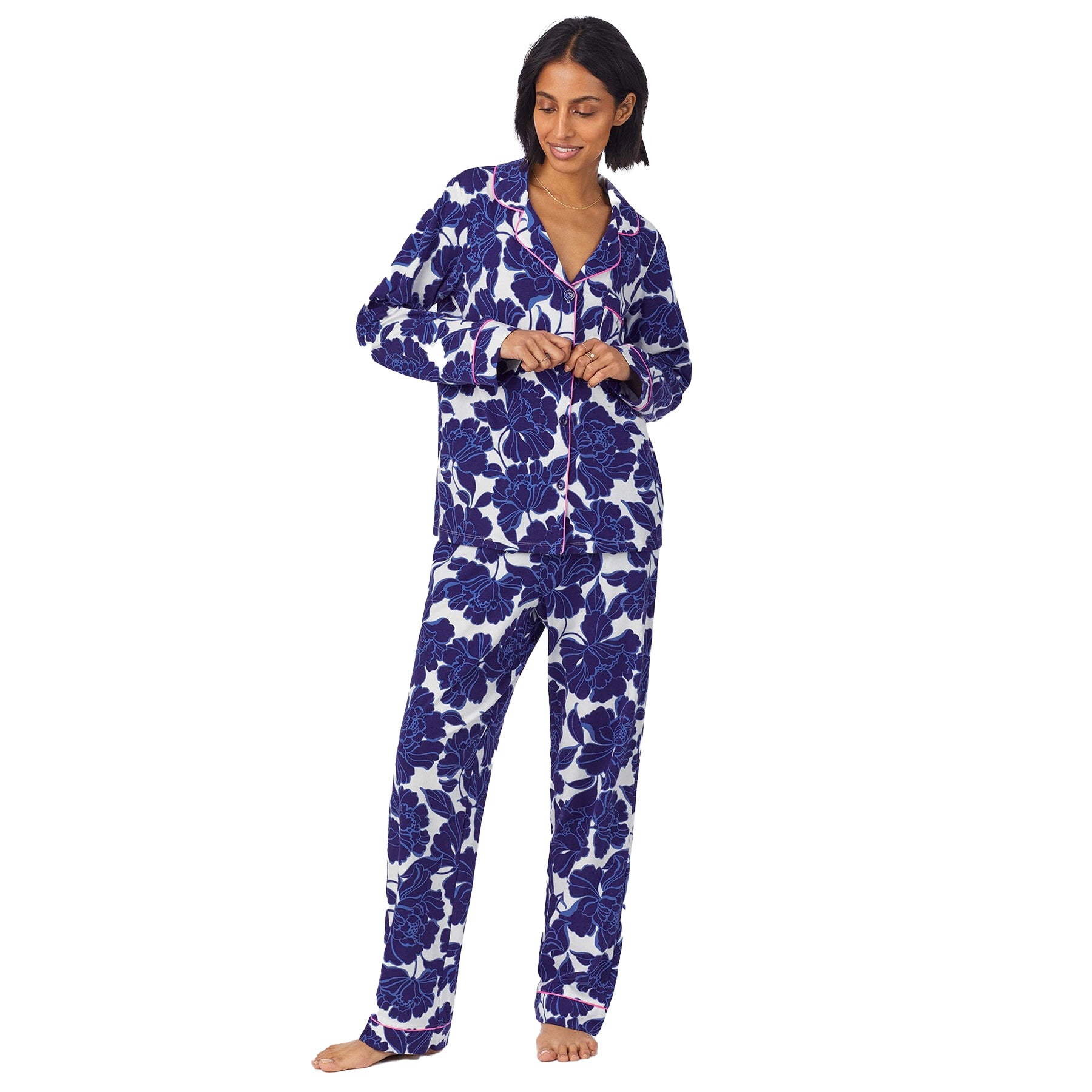 Full-length view of model buttoning the top of a floral pajama set, featuring a relaxed fit and classic collar.
