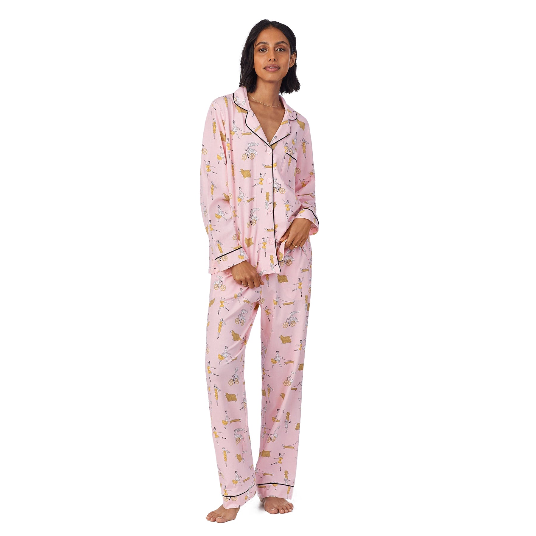Full-length view of a model in button-up pink pajama set, standing with one hand in pocket, showcasing a fun illustrated print.