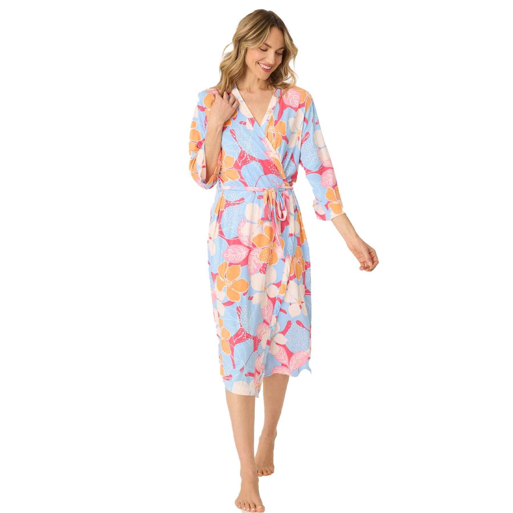 Woman walking forward, smiling and wearing a belted robe with colorful floral patterns on a white background.