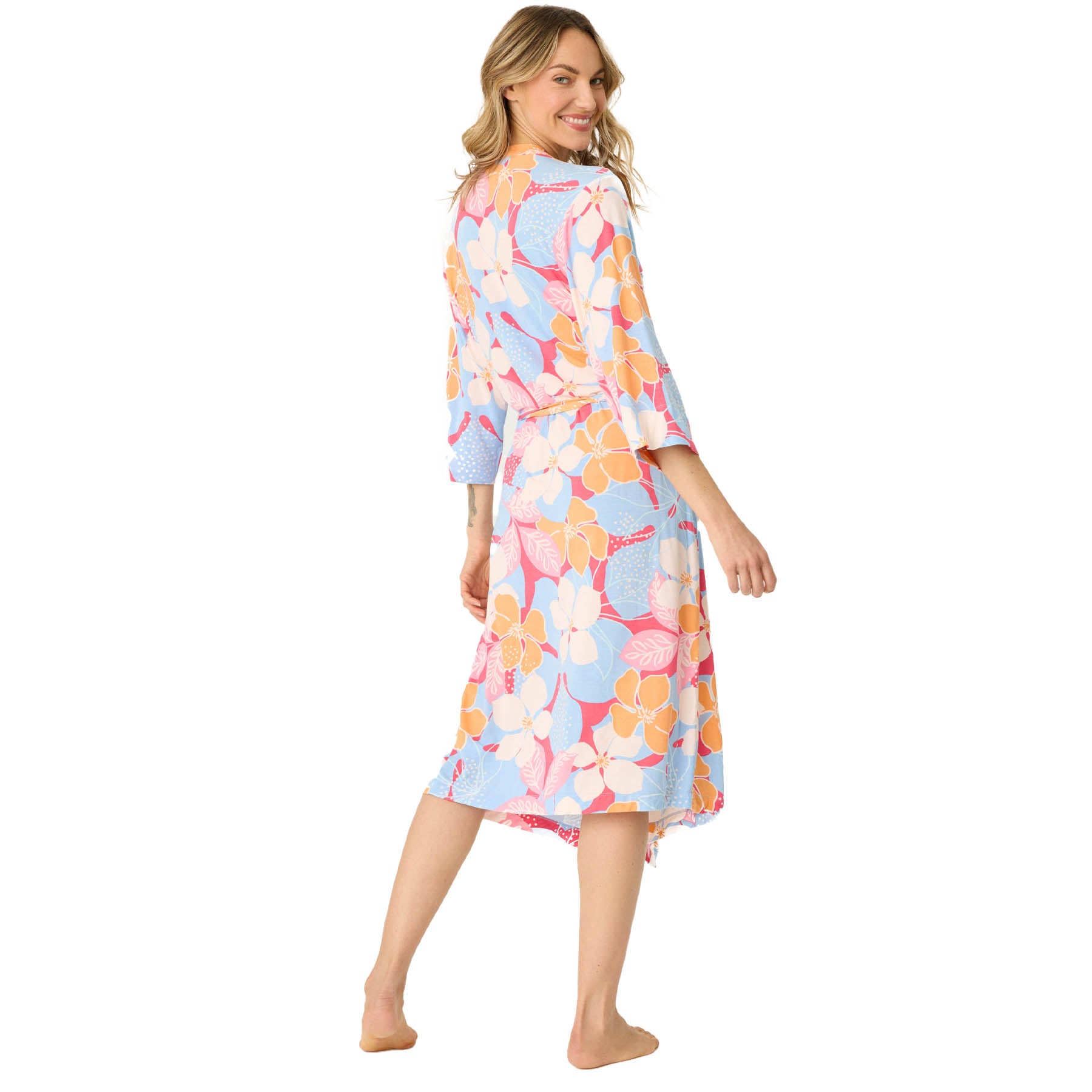 Woman standing barefoot and smiling over her shoulder in a mid-length floral robe, showing the back view.