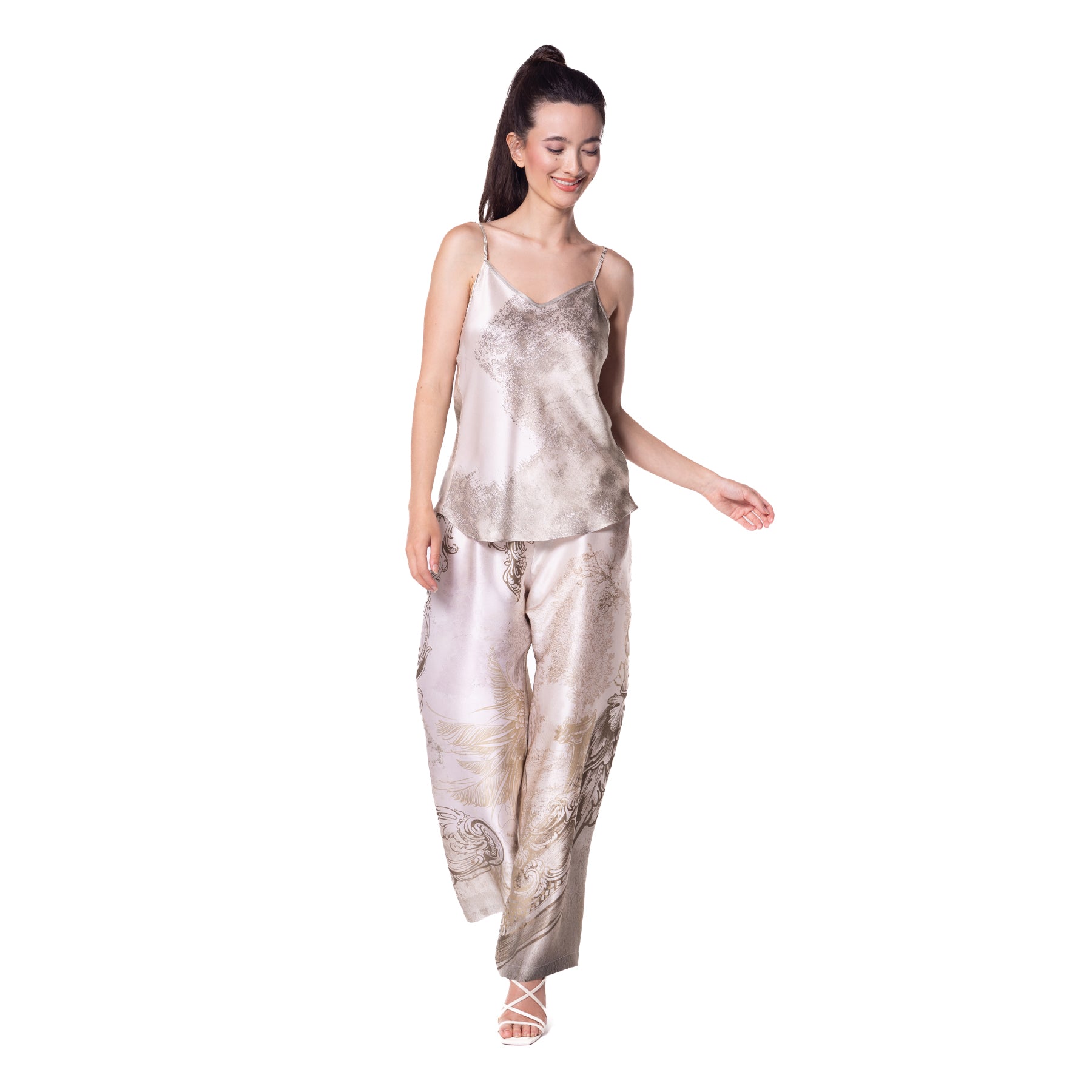 Woman wearing a luxurious satin pajama set with a subtle cloud-like print in neutral tones, smiling and walking forward.