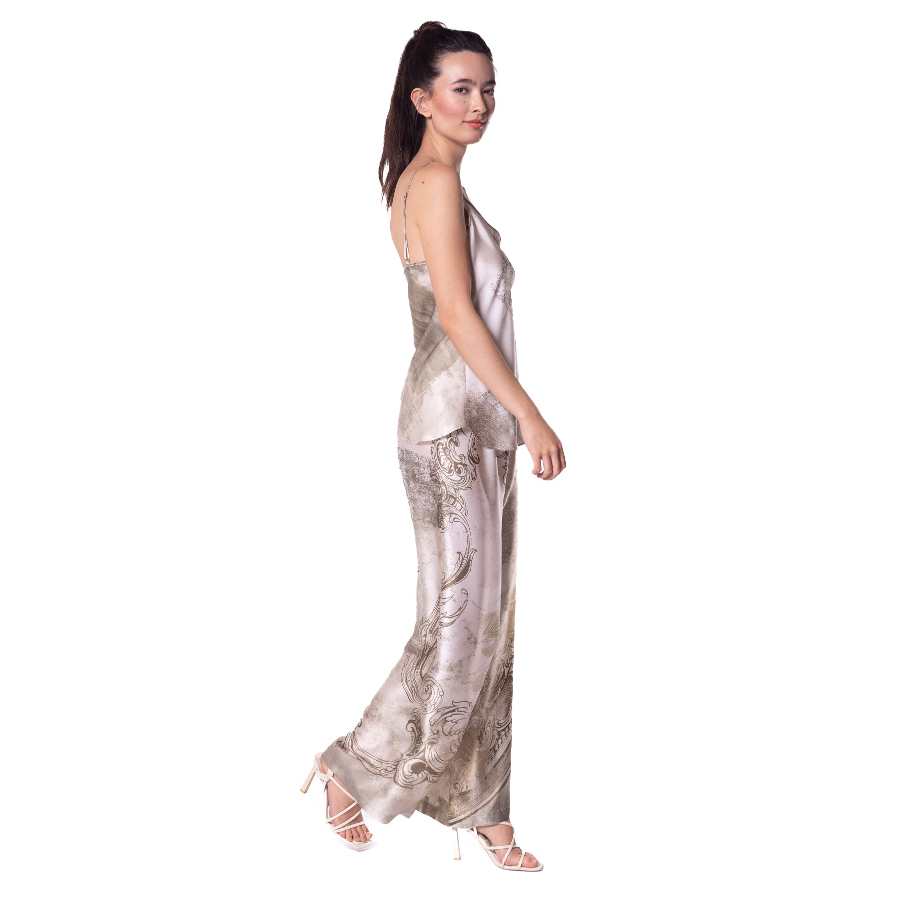 Side view of a woman modeling a satin pajama set with a soft, abstract landscape pattern in beige and gray hues.