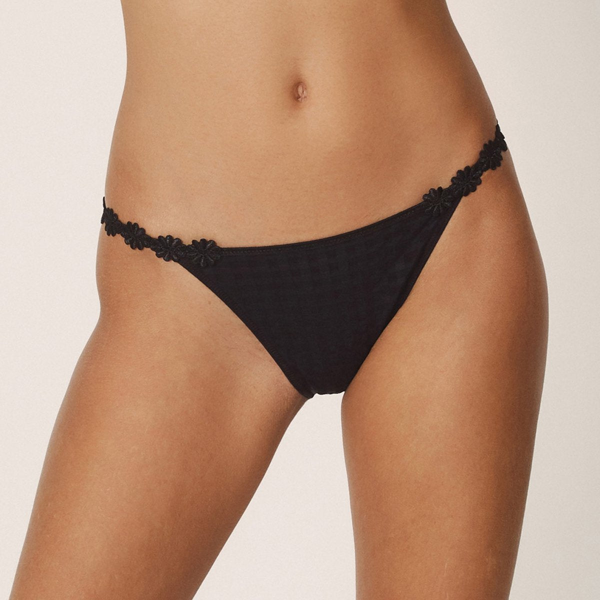 Low rise bikini panty in black with embroidered daisy string at hips. Front view on model.