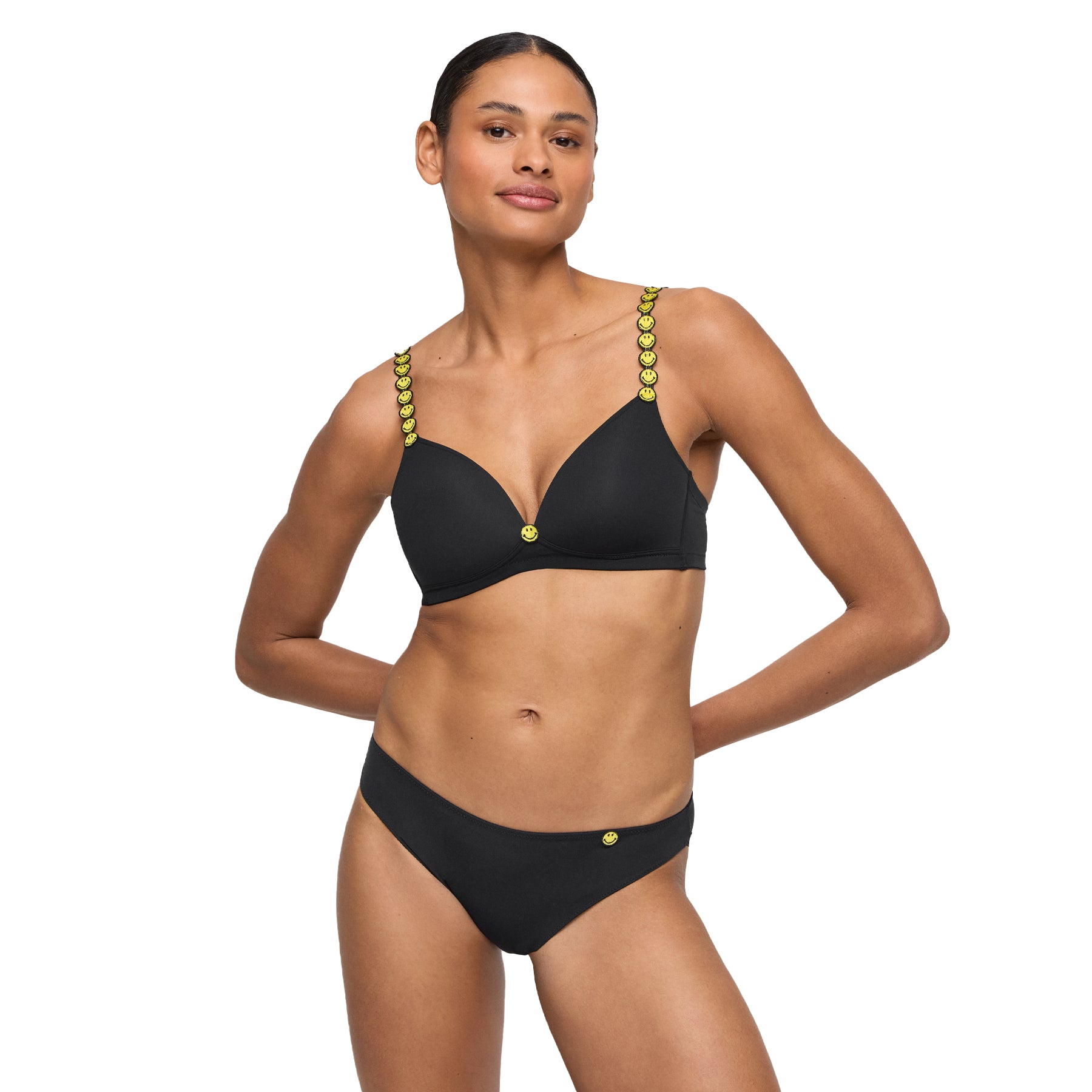Model wearing matching black bra and thong with yellow smiley details - front view.