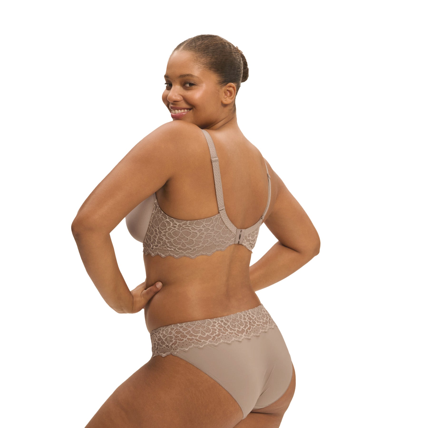 A model showing a grey/nude set of lacey basic lingerie from Simone Perele on a white background, back view.