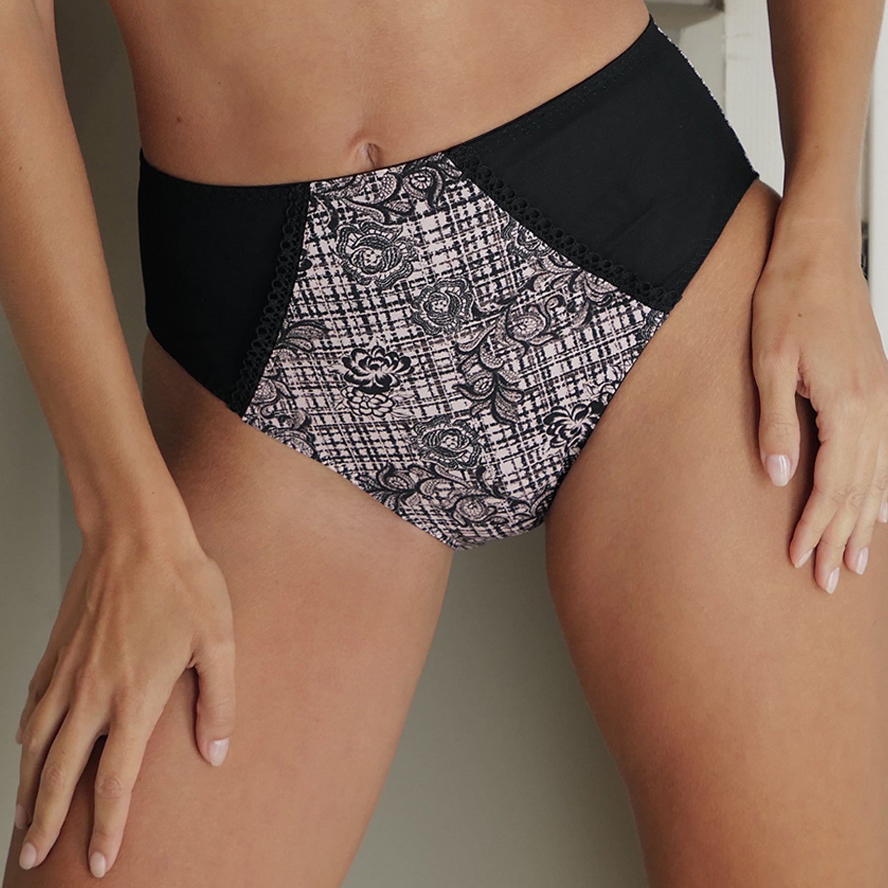 High waist full brief in black with a floral tartan print on a light pink background with black panels at front hips. Front view close up on model.