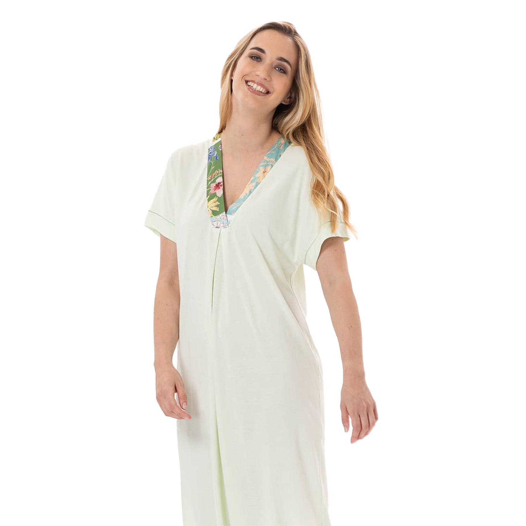 Side-front view of a woman smiling in a light green nightgown with a colorful floral V-neck detail and short sleeves.