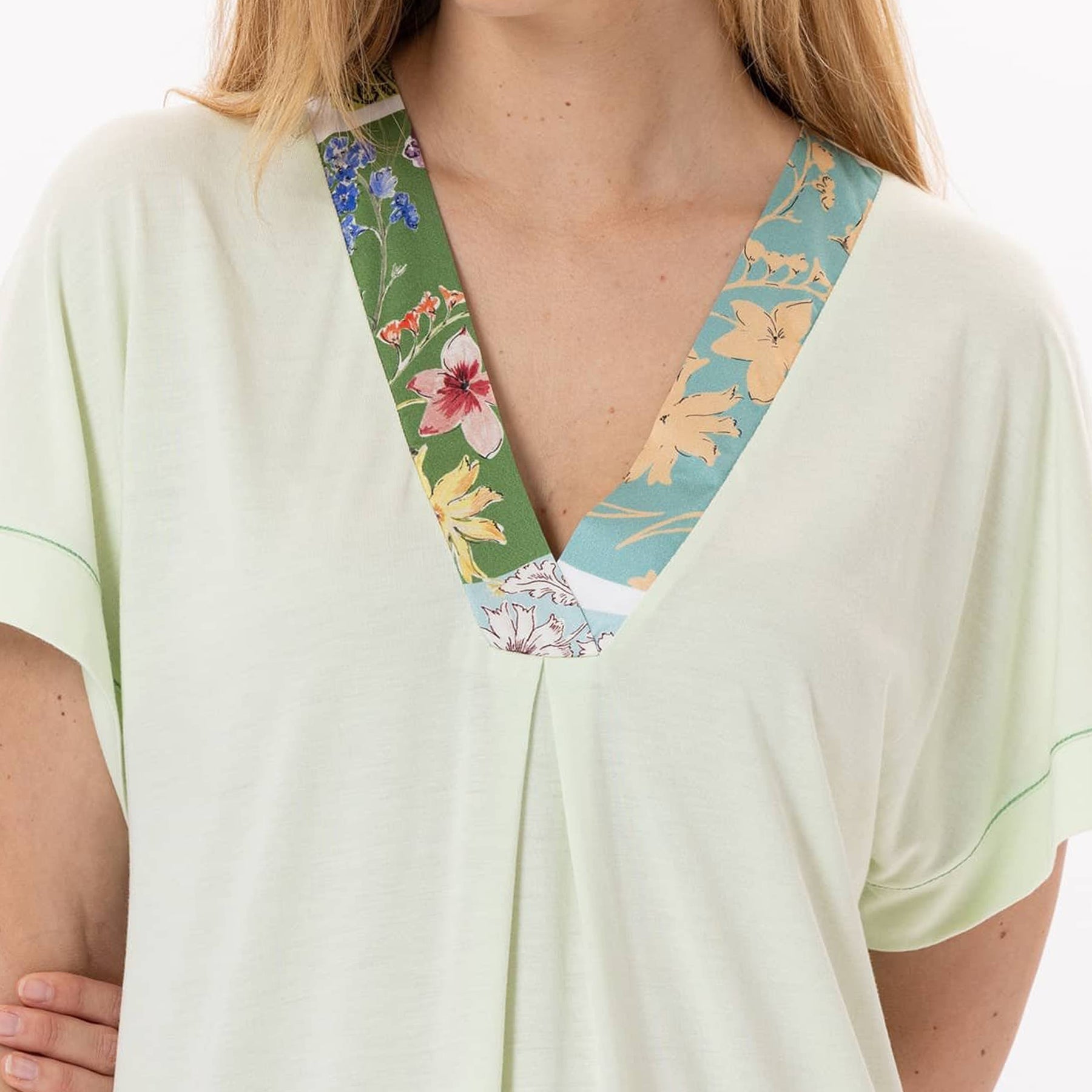 Close-up of the V-neckline on a light green nightgown, featuring contrasting floral patchwork trim in green, blue, and peach tones.