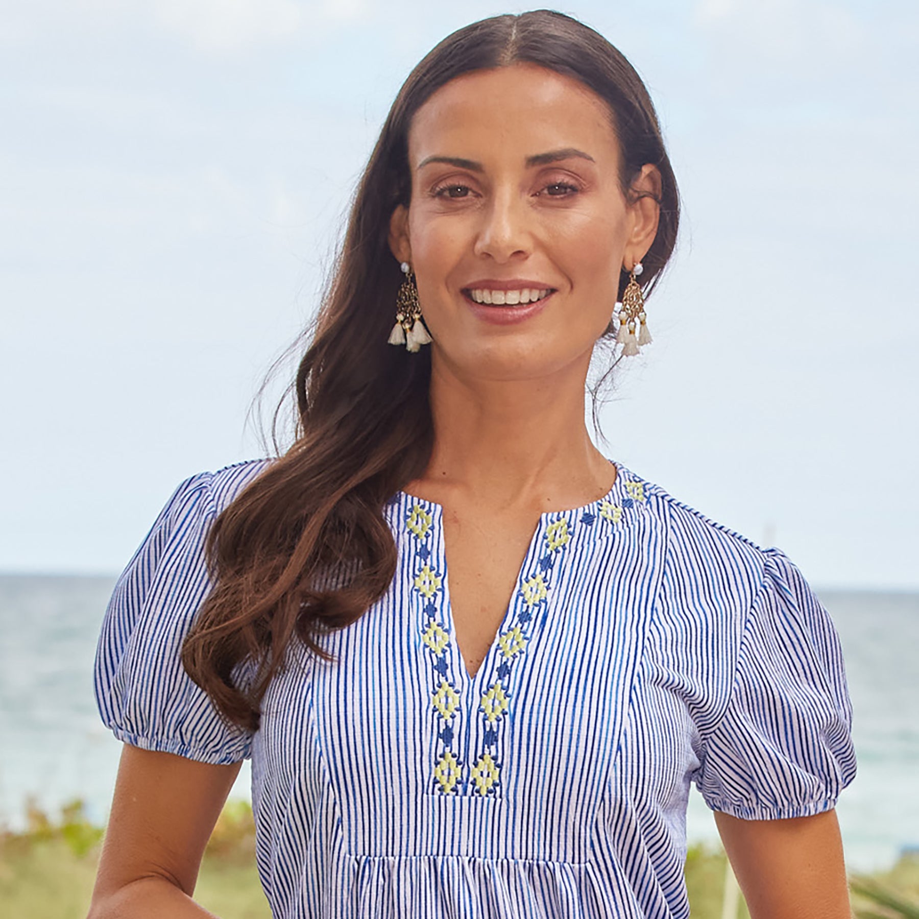 Blue and white striped puff short sleeve tiered dress with yellow and blue embroidery along the v-neck and ruffle hem. Front view close up on model.