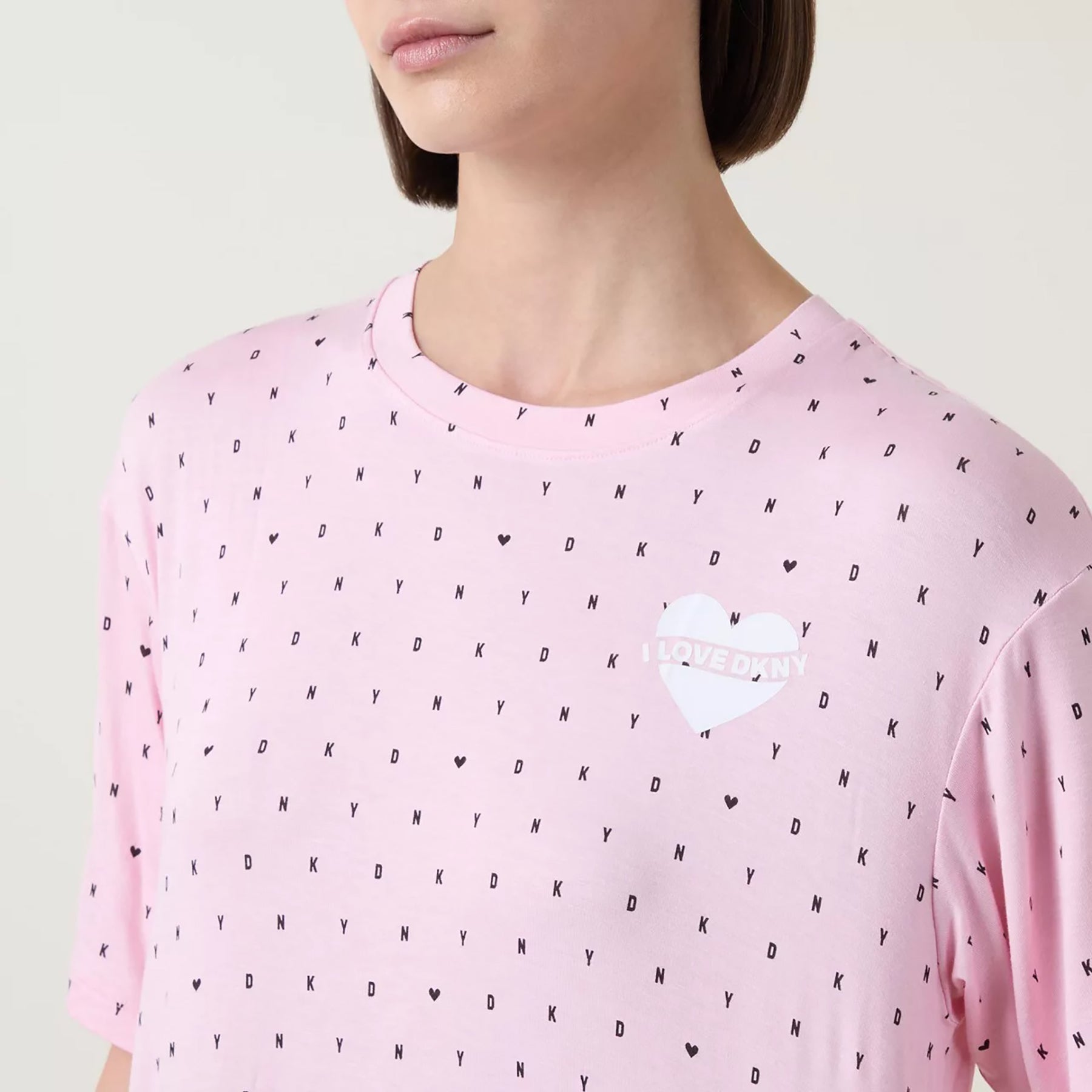 Short sleeve round neck sleepshirt in DKNY black mini logo and heart print on baby pink background. Front view close up on model.