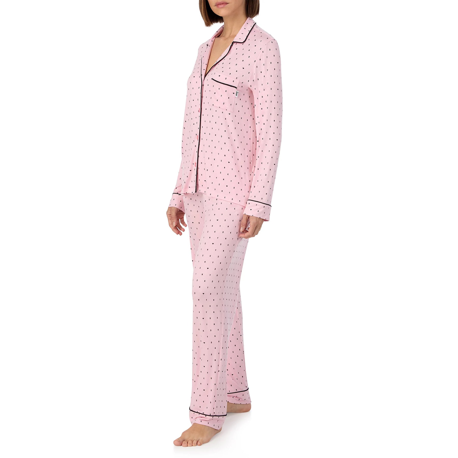 Classic button up 2-piece pyjama set in DKNY black mini logo and heart print on baby pink background. Side view on model.