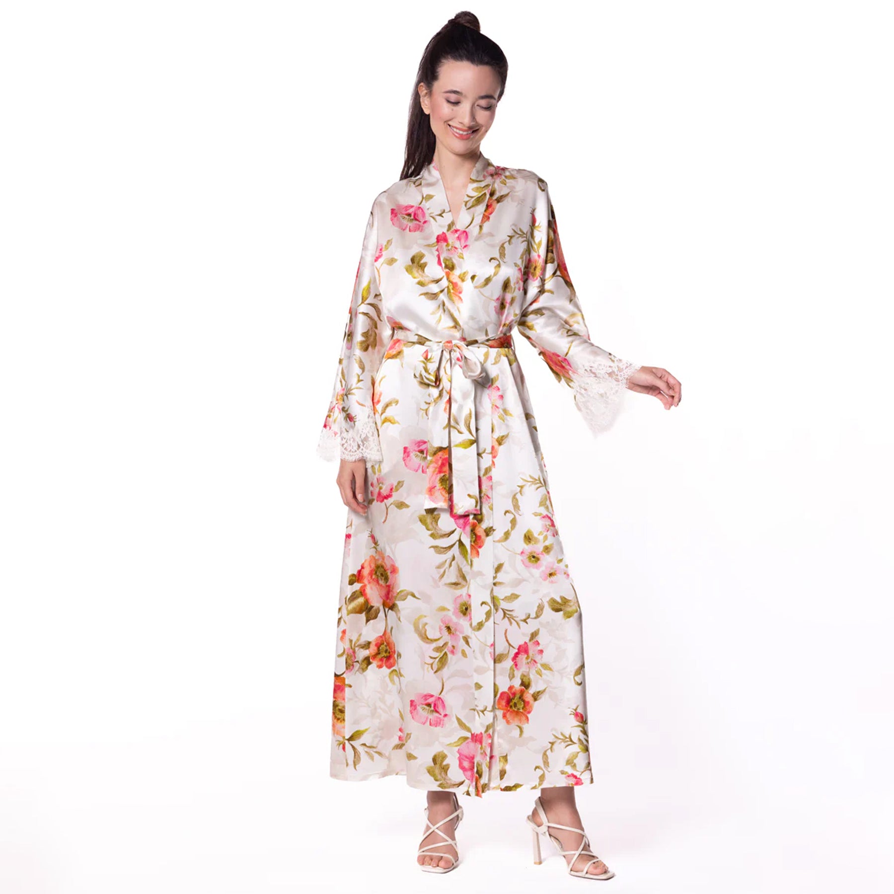 Woman wearing a full-length white silk robe with a vibrant pink and green floral print and lace-trimmed sleeves, tied at the waist.
