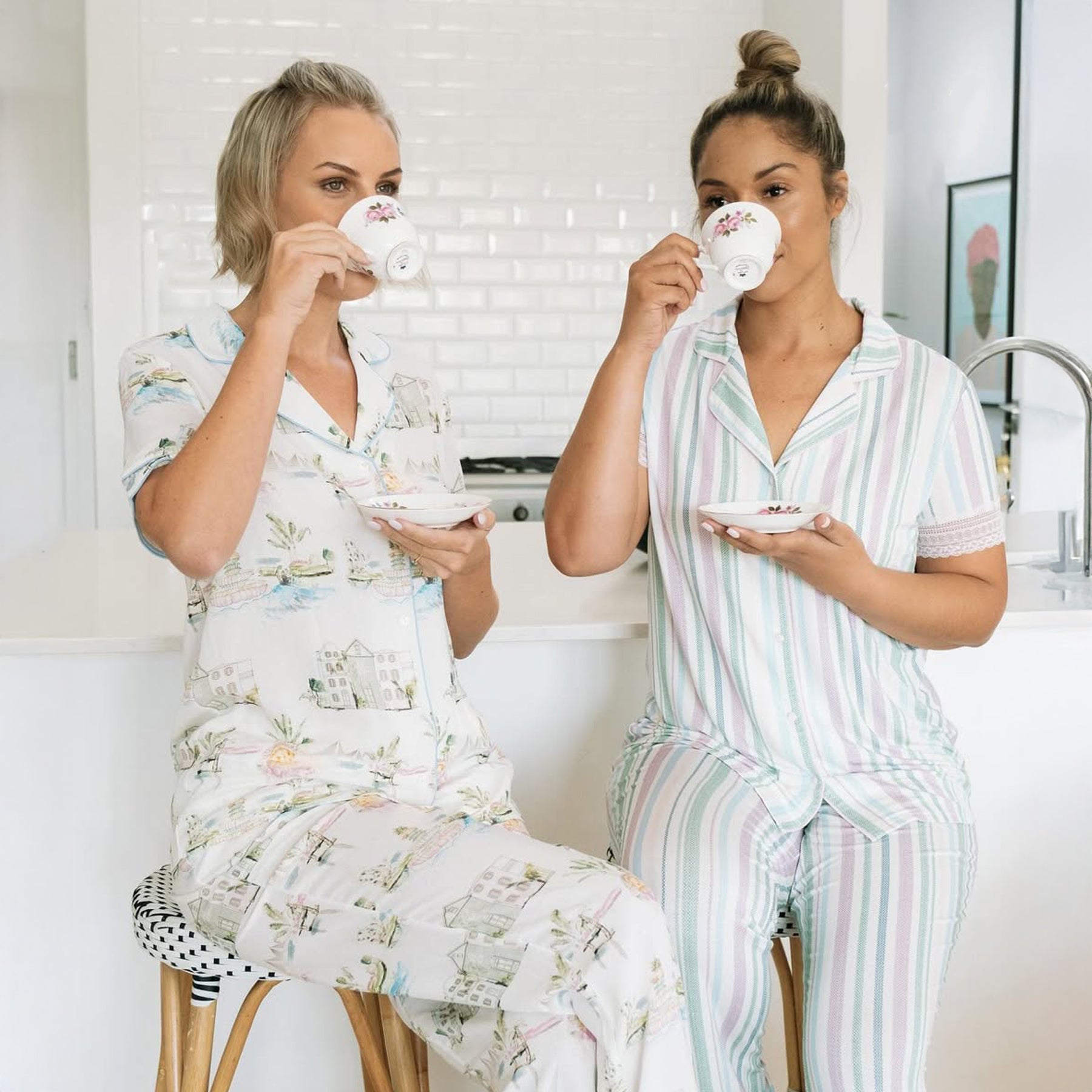 Two women sitting, drinking coffee in PJ Set in the kitchen. 