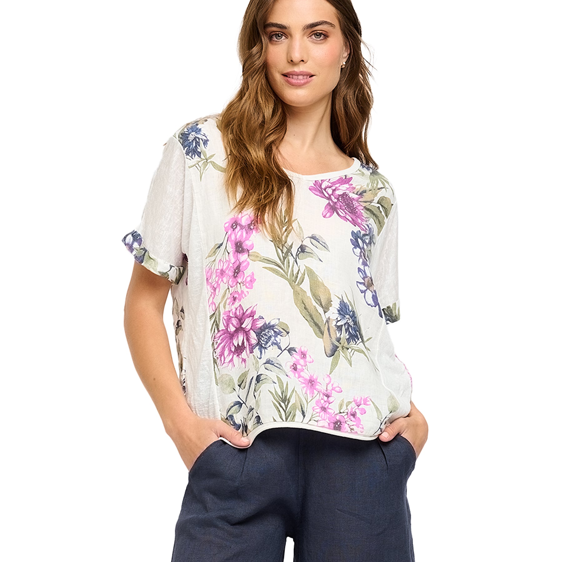 Woman wearing a short-sleeve white top with vibrant pink, purple, and blue floral print and rolled sleeves - lightweight Amalfi-inspired linen blend.