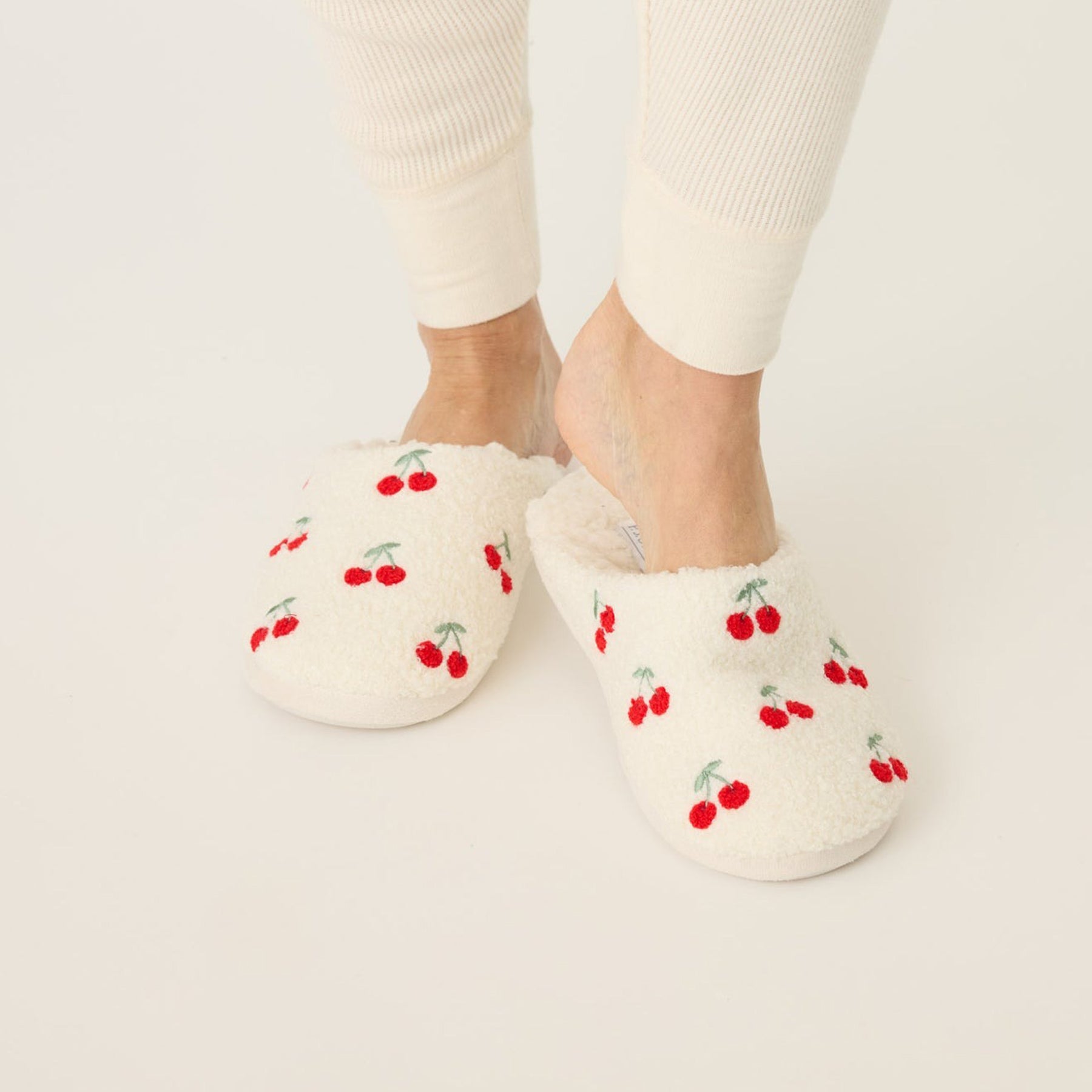 Fuzzy and fleecy slippers in ivory with red cherry print, front view.