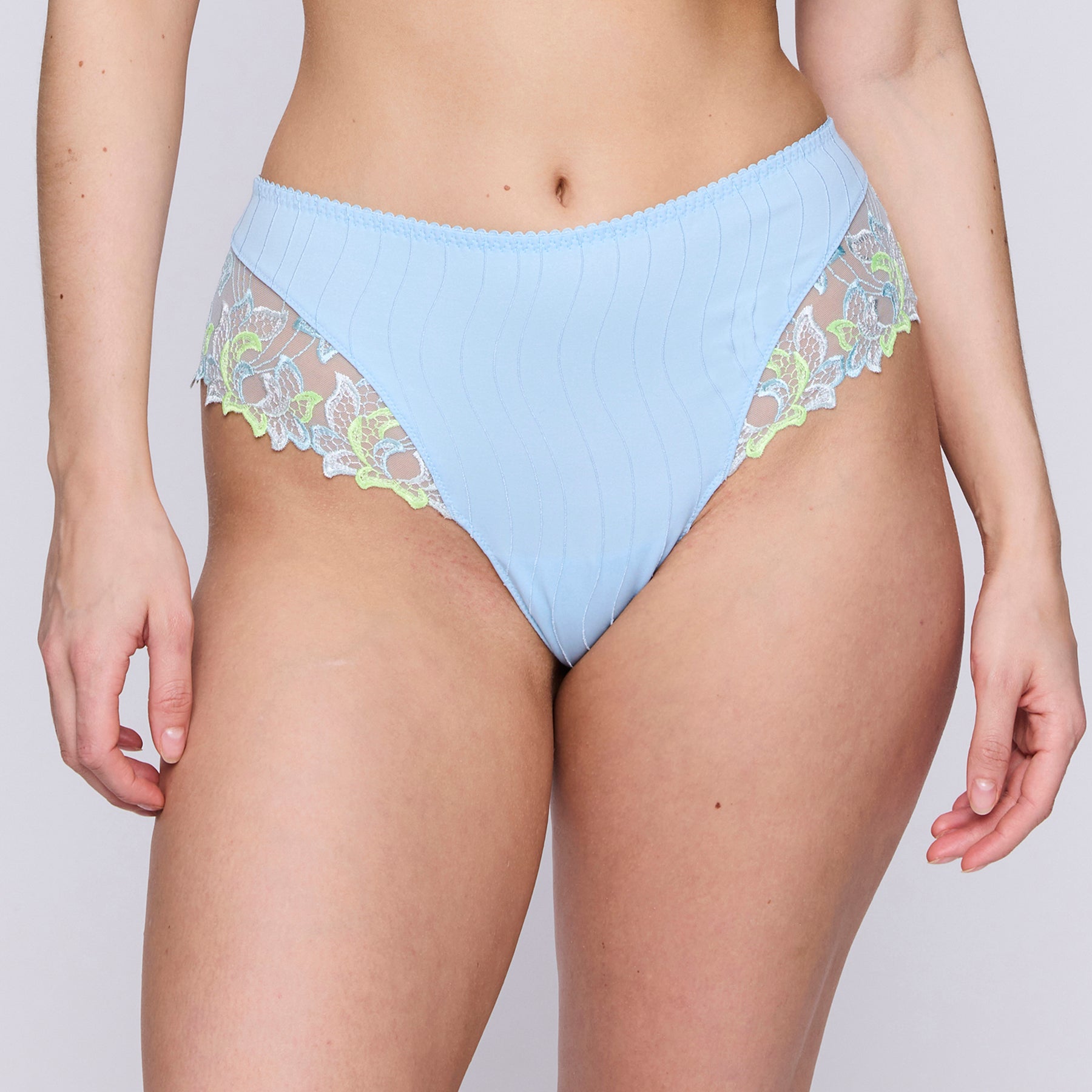 Luxury thong in milky baby blue with contrast lime green embroidery at hips and around the legs. Front view on model.