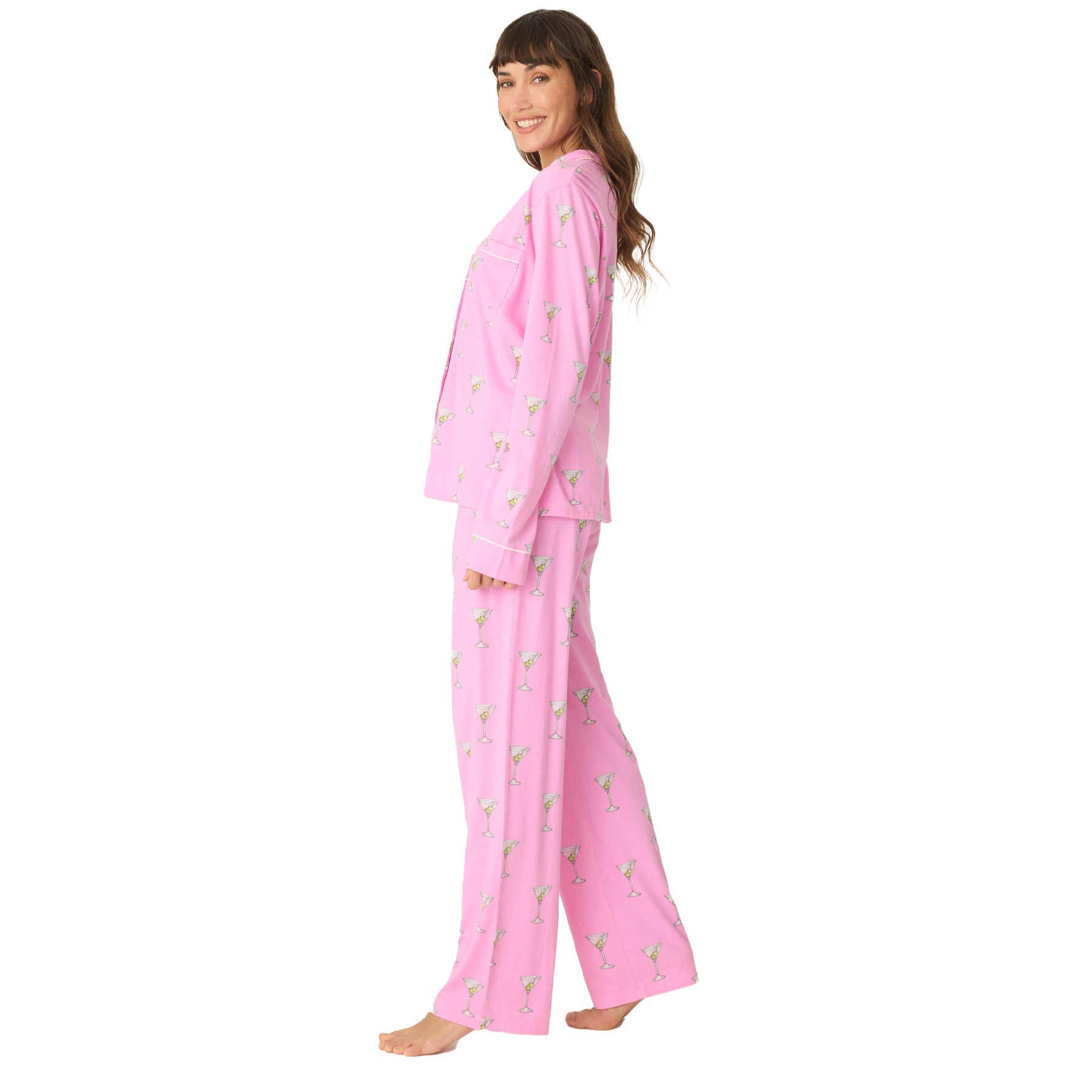 A side profile view of a woman wearing a pink martini-print pajama set, standing barefoot and smiling.