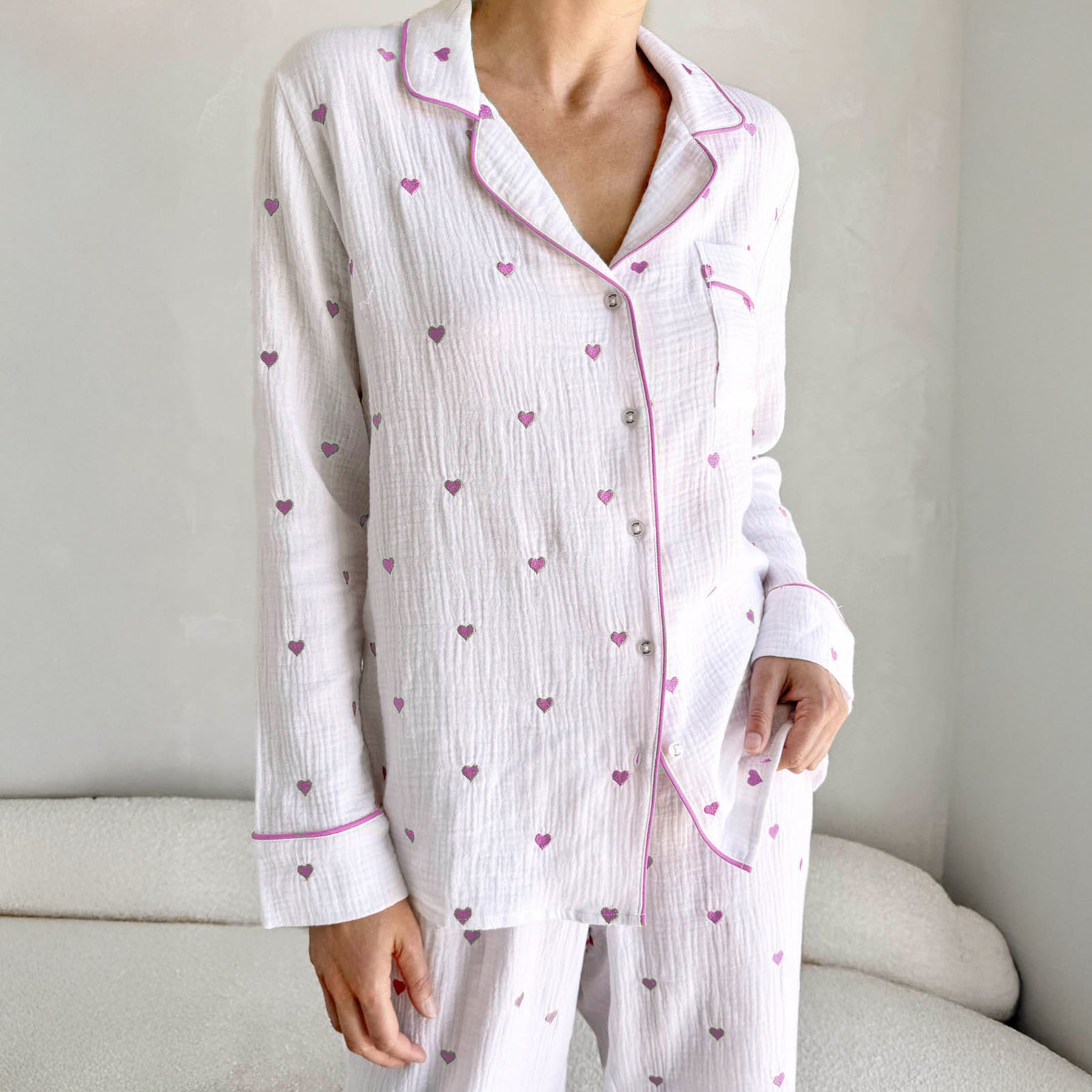 classic button up pyjama set in crinkle cotton in white with mini raspberry ice pink purple embroidered hearts. Matching raspberry ice pink purple contrast piping on trims. Front view close up on model.