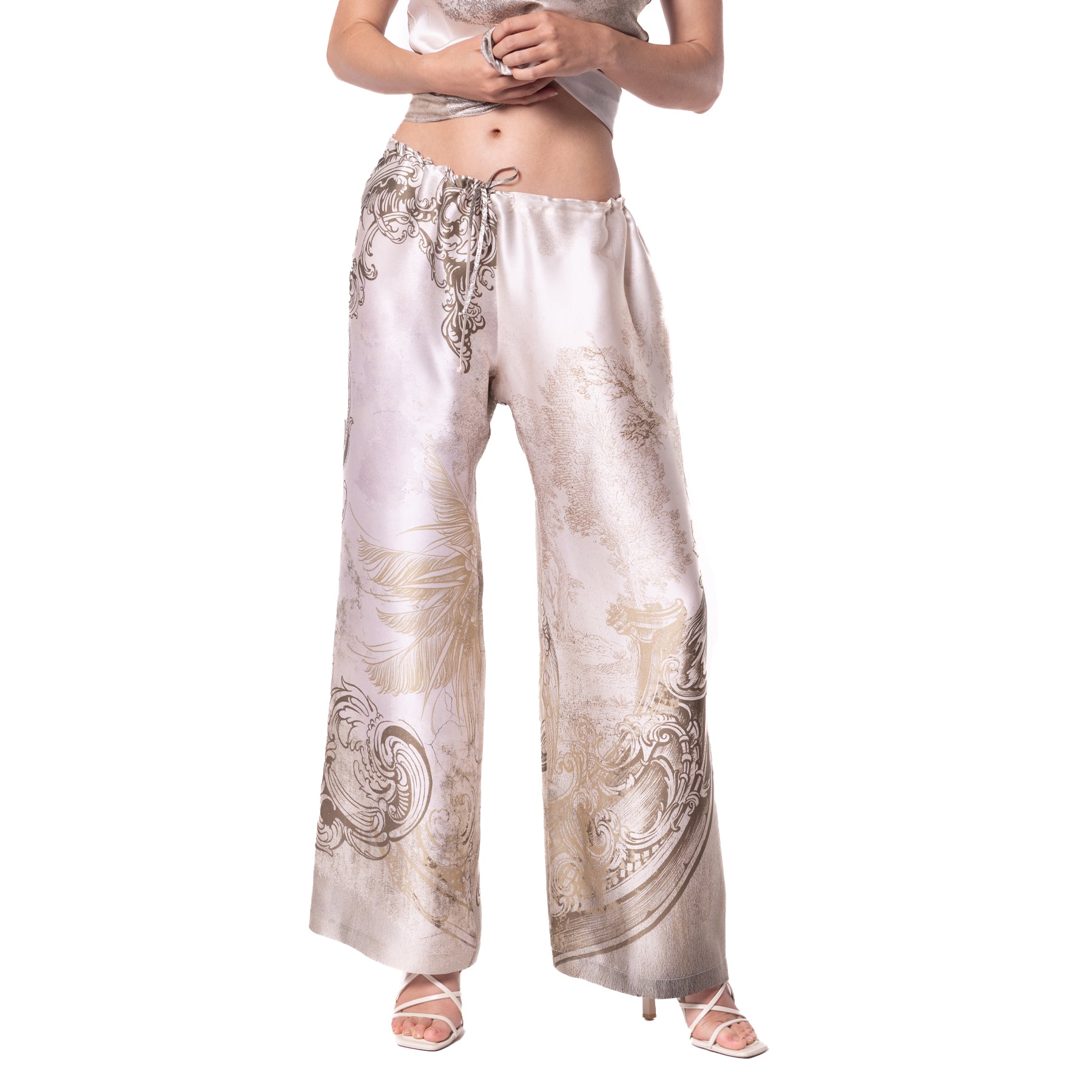 Close-up of wide-leg satin pajama pants featuring an ornate, baroque-inspired pattern in muted gold and gray.