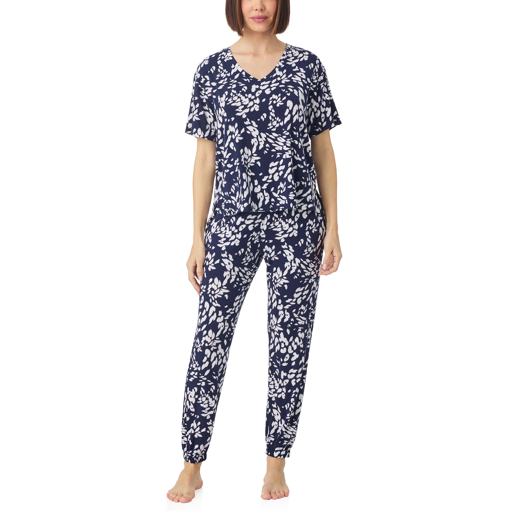 A full-body front view of a woman wearing a matching navy and white print pajama set, including a short-sleeve V-neck top and jogger pants.